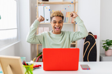 Excited young hispanic latin man celebrating good news using laptop at home. Euphoric winner happy...
