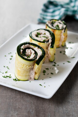 Grilled zucchini rolls stuffed with cream cheese and tuna on wooden table. Close up