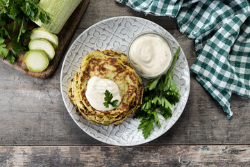 Zucchini fritters with yogurt sauce on wooden table. Top view