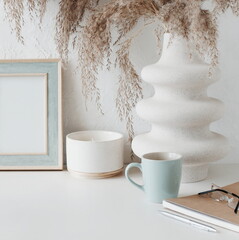 Modern women's home office workspace with photo frame mockup.  Aesthetic scandy hygge style.Cup coffee, photo frame,planner, vase with grass,aroma candle .Copy space.Neutral colors home design.