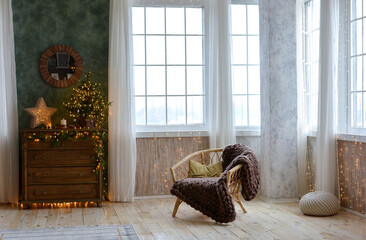 Interior of a beautiful Christmas room with a wooden chest of drawers , armchair, beautifully decorated Christmas tree on the chest of drawers by the window. Christmas decorations.