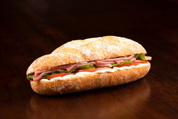 large smoked carpaccio sandwich with arugula tomato and gruiere cheese on italian baguette on wooden board and dark background angle view macro closeup from front ham