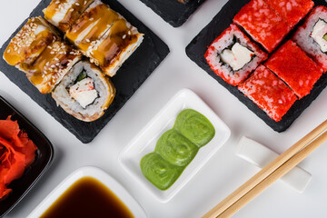 close-up, on a white table, on a black stand, assorted Japanese rolls with crab meat, cream cheese, eel and red caviar of flying fish and sauces, ginger, wasabi and wooden sticks