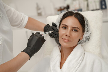 Cosmetologist makes rejuvenating anti wrinkle injections on face of woman in beauty salon