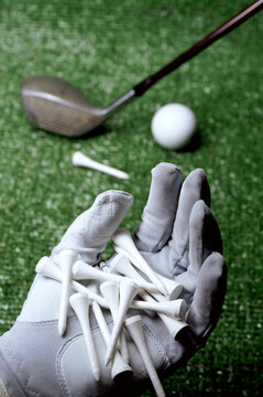 Person's gloved hand holding tees with a golf club and a ball in the background
