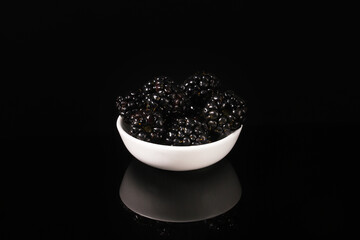 Fototapeta na wymiar Blackberries in a white plate on a dark table with reflection. Close-up
