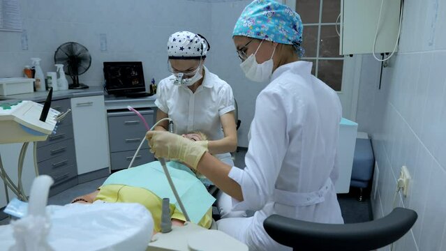 Young woman dentist, treats the teeth of a female patient.