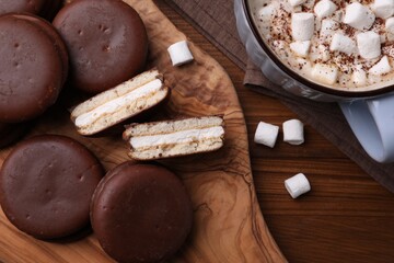 Tasty choco pies and cocoa with marshmallows on wooden table, flat lay