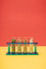Lab glass test tubes with colourful sugar candy sprinkles and medicine pills on a yellow and red background with copy space. Creative concept of overdose, placebo and addiction to food supplement.