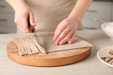 Woman making soba (buckwheat noodles) at wooden table, closeup