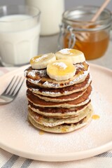 Plate of banana pancakes with honey and powdered sugar served on table, closeup