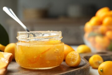 Delicious kumquat jam in jar and fresh fruits on wooden board, closeup. Space for text