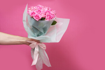 The male hand of the courier holds out a bouquet of roses on a pink background. With space to copy. High quality photo