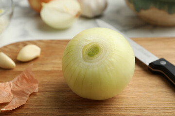 Peeled onion and knife on wooden board, closeup