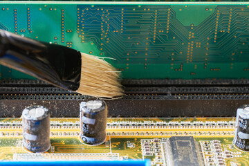 Brush cleaning an old motherboard from covering dust and dirt. Close-up.