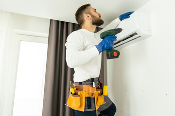 Male technician fixing air conditioner indoors.