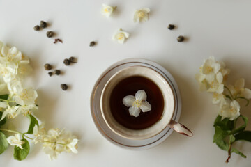 Obraz na płótnie Canvas Beautiful jasmine flowers and cup of aromatic tea on white table, flat lay
