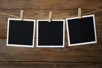 Clothespins with empty instant frames on twine against wooden background. Space for text