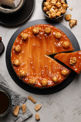 Sliced delicious caramel cheesecake with popcorn served on light grey table, flat lay