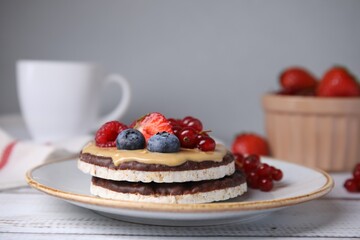Crunchy rice cakes with peanut butter and sweet berries served on white wooden table, closeup