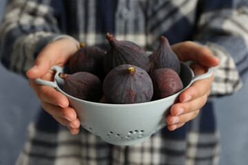 Woman holding colander with tasty raw figs on light blue background, closeup