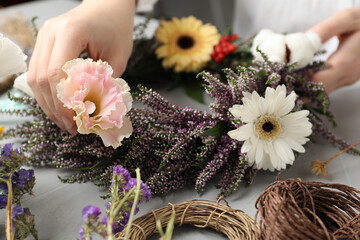 Florist making beautiful autumnal wreath with heather flowers at light grey table, closeup