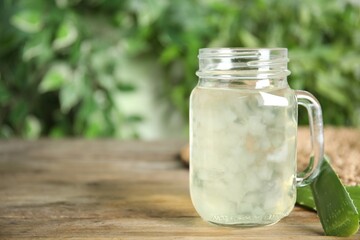Fresh aloe drink in mason jar and leaves on wooden table, space for text