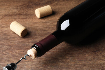 Opening wine bottle with corkscrew on wooden table, closeup