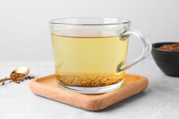 Cup of aromatic buckwheat tea and granules on light marble table, closeup