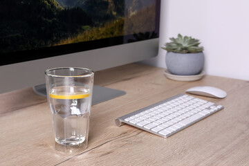 Glass of lemon water and modern computer on wooden table indoors