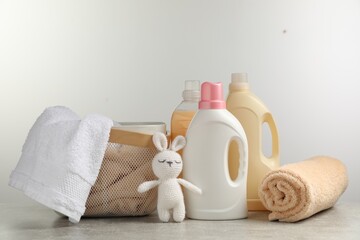 Obraz na płótnie Canvas Bottles of laundry detergents, fresh towels, knitted rabbit toy on grey table against white background