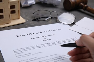 Woman signing last will and testament at grey table, closeup