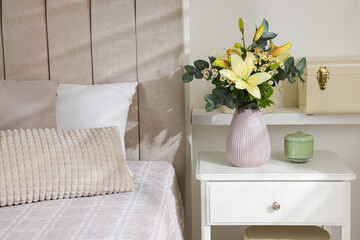 Stylish vase with flowers and decor on bedside table indoors. Bedroom interior elements