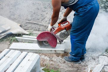 A worker mends part of the road, cuts out worn asphalt in a cloud of dust using a portable concrete...