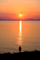 The silhouette of a man standing on the seashore during sunrise.