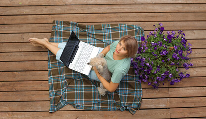 Top view of a woman sitting on the balcony with a laptop and a dog, hands on the keyboard, next to...