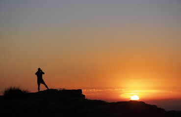 Hiker photographing the sunrise with his cell phone from the top of the mountain.