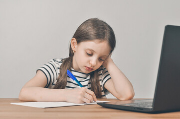 Naklejka premium European girl with a laptop. Sitting at the table doing homework. Online learning