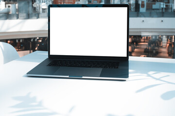 Laptop mockup with white screen in business office or shopping mall. Empty copy space, blank screen mockup. Soft focus laptop with interor background. Travel, study and office work concept