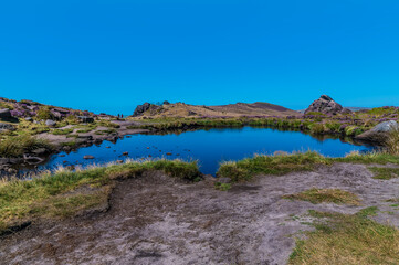 Fototapeta na wymiar A view across Doxey Pool looking towards the cliff edge on the summit of the Roaches escarpment, Staffordshire, UK in summertime