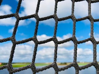 The mesh of a net against blue sky with white clouds