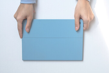 A tablet in a blue case on a white desk. The girl's hands are holding a tablet. top view