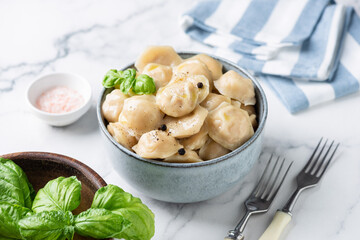 Meat stuffed Tortellini or Dumplings or Pelmeni served in a bowl with butter and basil, white marble background