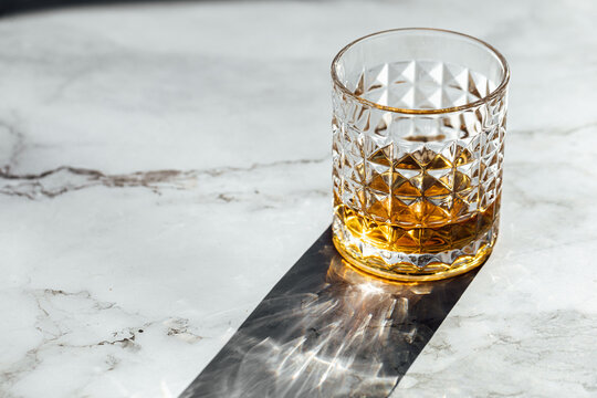 photography of scotch whisky glass in a marble table with light and shadow