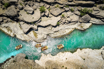 White water rafting.  Adventure and sport. A group of four yellow rafts floating among the rocks on the crystal clear, blue-green water. Perpendicular drone view of the rafters floating on Vjosa river