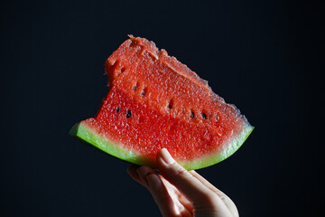 A slice of watermelon in your hand on a dark background. A slice of watermelon. 