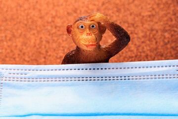 Figurine of a monkey behind a medical surgical mask. The concept of smallpox or monkeypox. Background with copy space