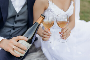 Close up cropped unrecognizable groom and bride hands drinking and pouring bubbly champagne wine from bottle and glasses