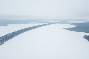 View from a height of a winter landscape with a snowy field, forest and fog