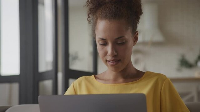 Close up portrait of an excited young adult African American woman reading good news on her laptop